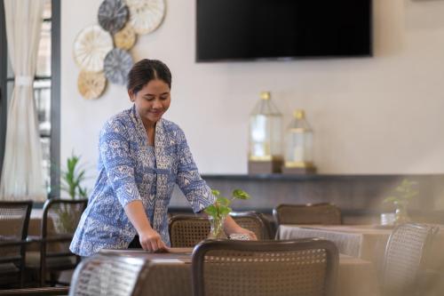una mujer está sentada en una mesa con una planta en The Margaux Hotel Yogyakarta, en Yogyakarta