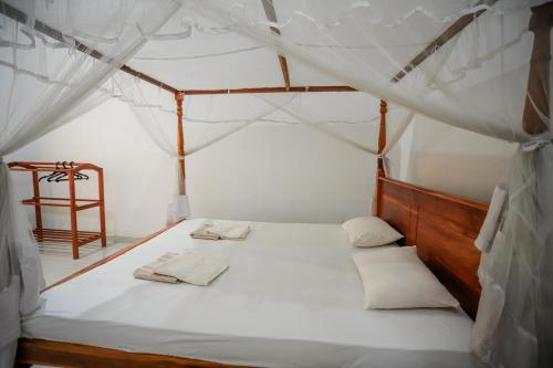 ein Schlafzimmer mit einem Himmelbett mit weißer Bettwäsche und Kissen in der Unterkunft Serene Home Stay in Udawalawe