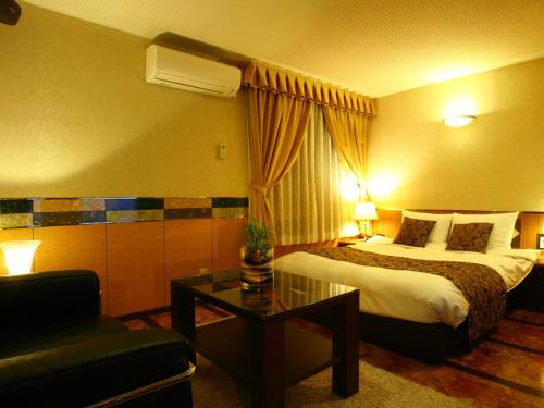 鳥栖市にあるHOTEL Villamure ogoriのベッド、テーブル、ソファが備わるホテルルームです。