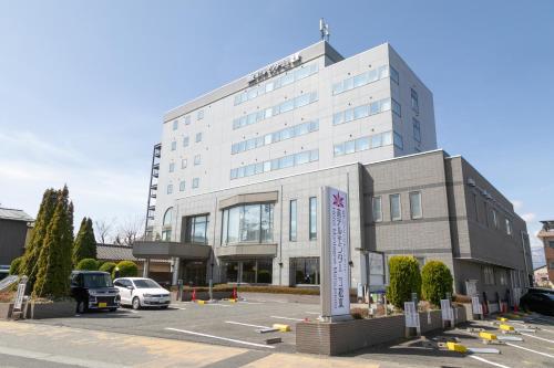 a large white building with cars parked in a parking lot at Hotel Montagne Matsumoto in Matsumoto