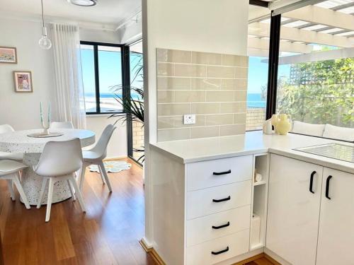 a kitchen with white cabinets and a dining room with a table at Dolce Vista - North Beach Coastal Haven in Perth