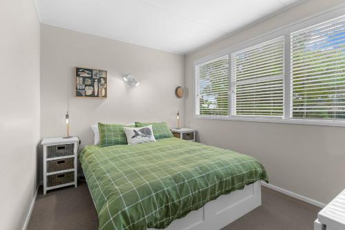 a bedroom with a green bed and a window at Sunseeker Cottage - Mangawhai Heads Holiday Home in Mangawhai