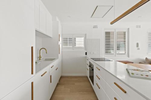 uma cozinha branca com balcões brancos e um lavatório em Stunning 2-Bed Coastal Pad Across From the Beach em Sydney
