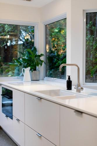 a white kitchen with a sink and two windows at Kate Owen Art House in Hobart