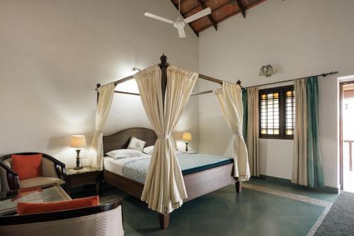 ウドゥピにあるBalkatmane Heritage Spa Resort Udupiのベッドルーム(天蓋付きベッド1台、椅子付)