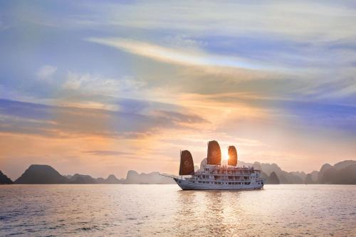 un bateau avec deux voiles sur l'eau au coucher du soleil dans l'établissement Hera Cruises Group on Ha Long Bay, à Hạ Long