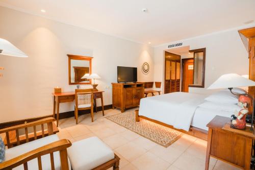 een slaapkamer met een wit bed en een televisie bij Ramayana Suites and Resort in Kuta