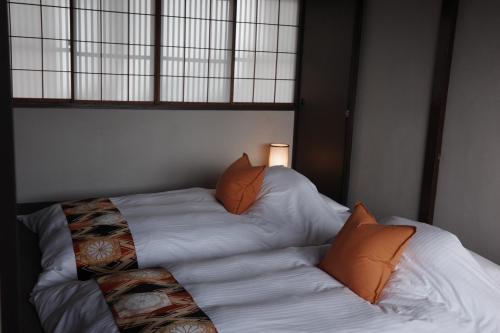 a bed with white sheets and orange pillows at 三間屋 mitsumaya in Kanazawa