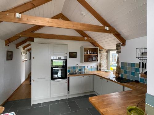 cocina con armarios blancos y vigas de madera en Trengothal Barn, en Porthcurno