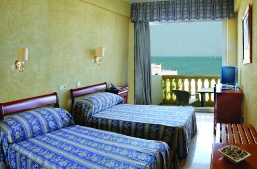 a hotel room with two beds and a balcony at Hotel Al Sur De Chipiona by YouRoom in Chipiona