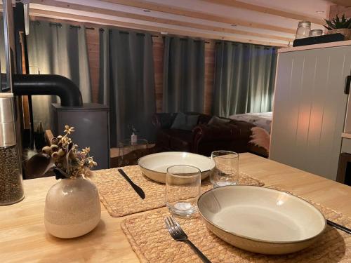 a wooden table with two plates and glasses on it at Cabane bien belge avec cinéma et jacuzzi in Lasne