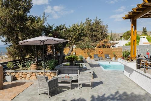 a patio with chairs and an umbrella and a pool at Villa Perla in Lardos