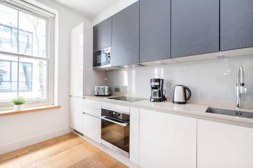 a kitchen with white cabinets and a sink and a window at Central London Soho Suite - CityApartmentStay in London