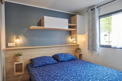 een slaapkamer met een bed met blauwe lakens en een raam bij Siblu Camping Meerwijck in Kropswolde