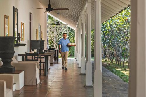 a man walking down a hallway with a tray of food at Uga Riva - Negombo in Negombo