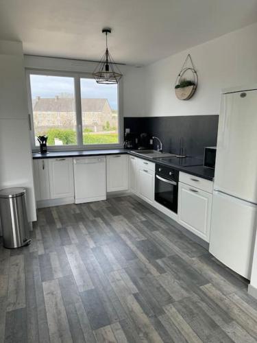 une cuisine avec des placards blancs et une grande fenêtre dans l'établissement Maison La méduse, à Quettehou