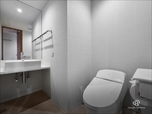 a white bathroom with a toilet and a sink at Daiwa Roynet Hotel Okinawa-Kenchomae in Naha