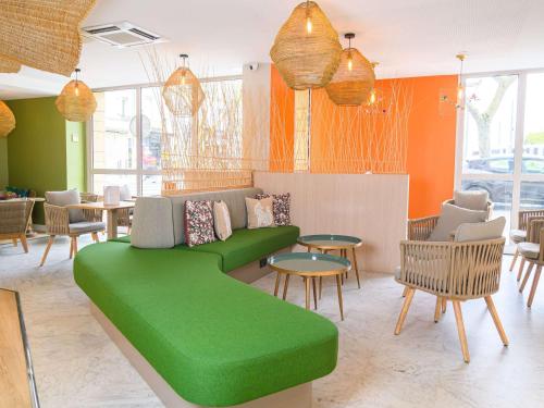 a green couch in a room with tables and chairs at ibis Styles Tours Centre in Tours