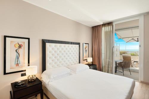 a white bedroom with a large bed and a balcony at Hotel Excelsior in Marina di Massa