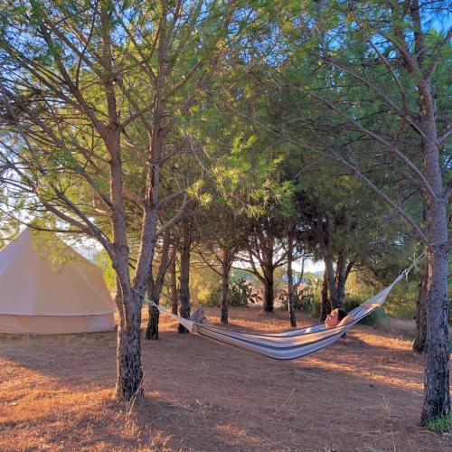 a person laying in a hammock between two trees at Glamping with Yoga and Natural Pool near Fuseta Beach in Moncarapacho