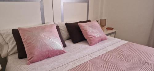 Una cama con dos almohadas rosas encima. en Parque don Jose, en Costa del Silencio