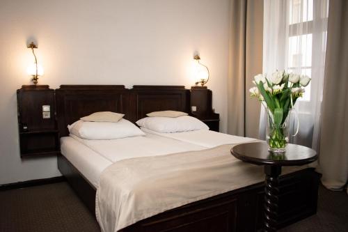 1 dormitorio con 1 cama con un jarrón de flores sobre una mesa en Hotel Dwór Polski en Breslavia