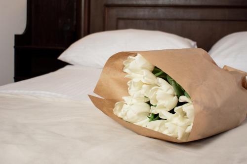 a bouquet of white flowers in a paper bag on a bed at Hotel Dwór Polski in Wrocław