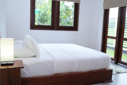 1 cama blanca en un dormitorio con ventanas en J Villa, en Gampaha