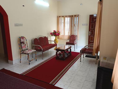 a living room with red chairs and a table and a red rug at Maria Vilas in Tirunelveli