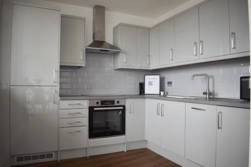 a white kitchen with white cabinets and a sink at Beautiful two bedroom with balcony in Brentwood in Brentwood