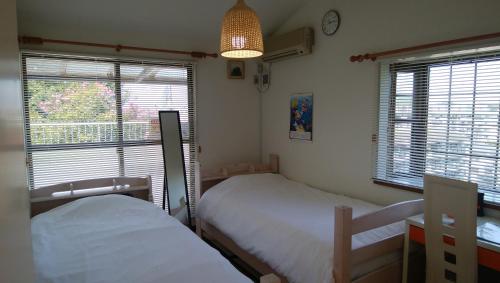 a bedroom with two beds and a desk and windows at Hostel Kamakura in Kamakura