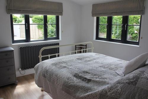 a white bedroom with a bed and three windows at The Pitstop in Sidlesham