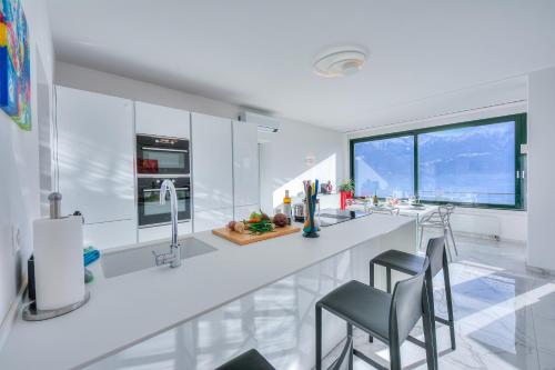 a white kitchen with a large white counter and chairs at Wonderful Blick Apartment Orselina - Happy Rentals in Orselina