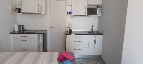 a small kitchen with white cabinets and pink shoes at Sunrise Studio Miro, vistas jardín y mar in Miami Platja
