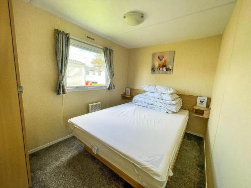 a small bedroom with a white bed with a window at Great Caravan At Valley Farm Holiday Park, Essex Ref 46583v in Great Clacton