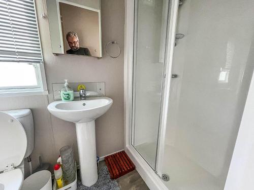 a man in a bathroom with a sink and a shower at Stunning 6 Berth Caravan At Suffolk Sands Holiday Park Ref 45031g in Felixstowe