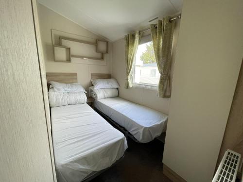 two beds in a small room with a window at Wonderful 8 Berth Caravan With Wi-fi And Decking At Seawick, Ref 27023sw in Clacton-on-Sea