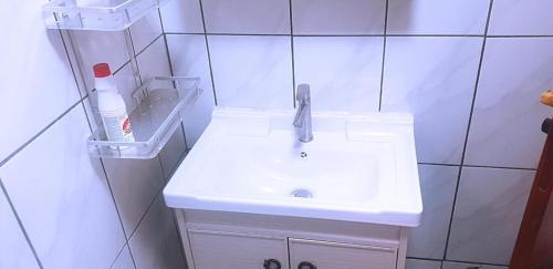a white sink in a white tiled bathroom at Le meublé des voyageurs in Yaoundé