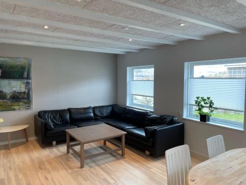 a living room with a black leather couch and two windows at New apartment in the middle of Klaksvík in Klaksvík
