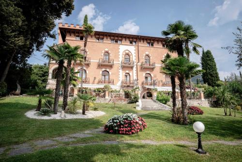 un gran edificio de ladrillo con palmeras y flores en Hotel Bellevue, en Gardone Riviera