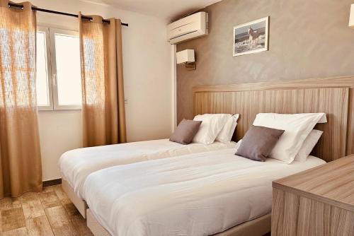 two beds in a hotel room with a window at Hotel Les Palmiers En Camargue in Saintes-Maries-de-la-Mer