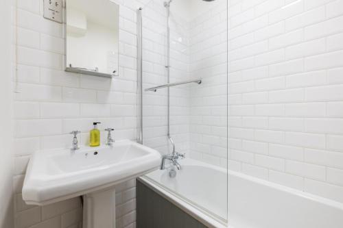 La salle de bains blanche est pourvue d'un lavabo et d'une douche. dans l'établissement Olympia's Torch 1 Bedroom in Kensington, à Londres