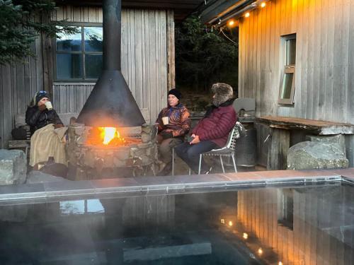 a group of people sitting around a fireplace next to a pool at Luxury Lakefront villa, infinity hot tub and sauna in Grímsnes og Grafningshreppur