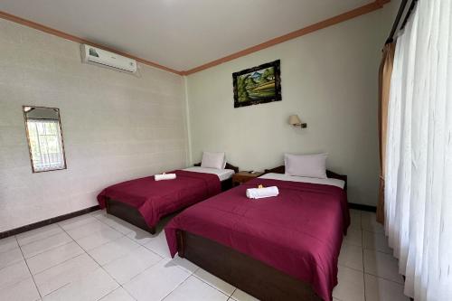 two beds in a small room with red sheets at Taxa Raya Guest House in Legian