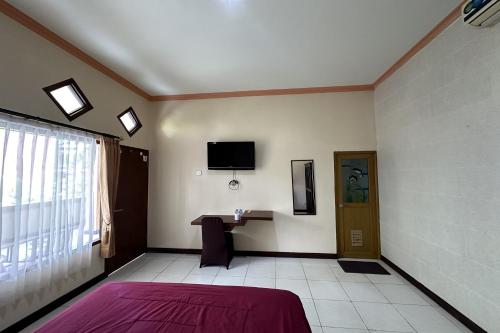 a room with a bed and a table and a tv at Taxa Raya Guest House in Legian