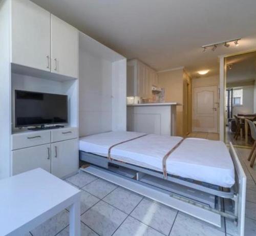 een witte kamer met 2 bedden en een keuken bij Studio Sia - Lichtrijke studio met balkon met zijzeezicht in hartje de Panne in De Panne