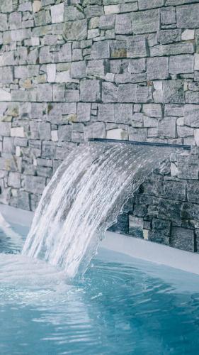 une cascade en face d'un mur en pierre à côté d'une piscine dans l'établissement Villa des Dunes, à La Tranche-sur-Mer