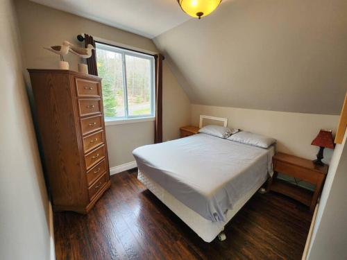 a bedroom with a bed and a dresser and a window at The Hidden Porch at Sir Sam's (hot tub & sauna) in Haliburton