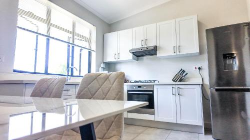 a kitchen with white cabinets and a stainless steel refrigerator at Impeccable Apartment in Victoria Falls 128 TheYard in Victoria Falls