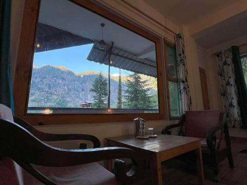 a room with a table and a large window at Rishi Villa in Manāli